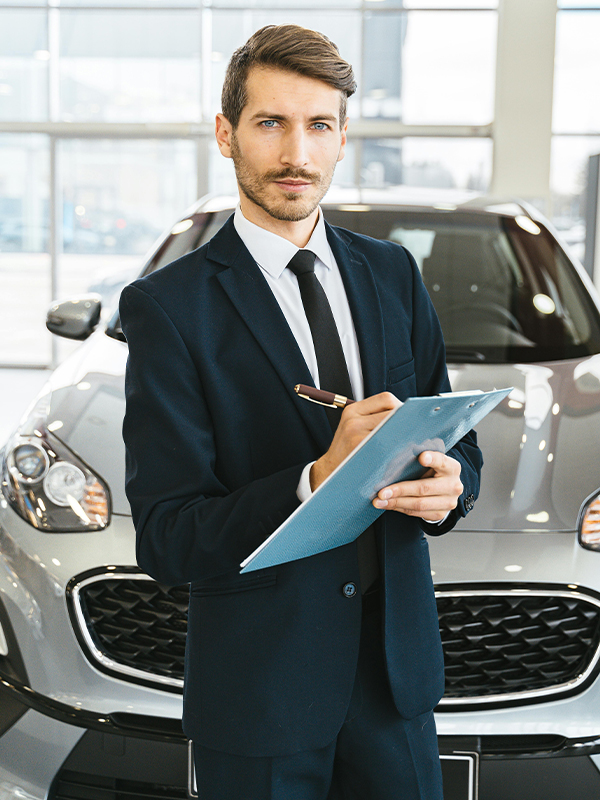 Salesman in auto dealership with car in background while he signs contract
