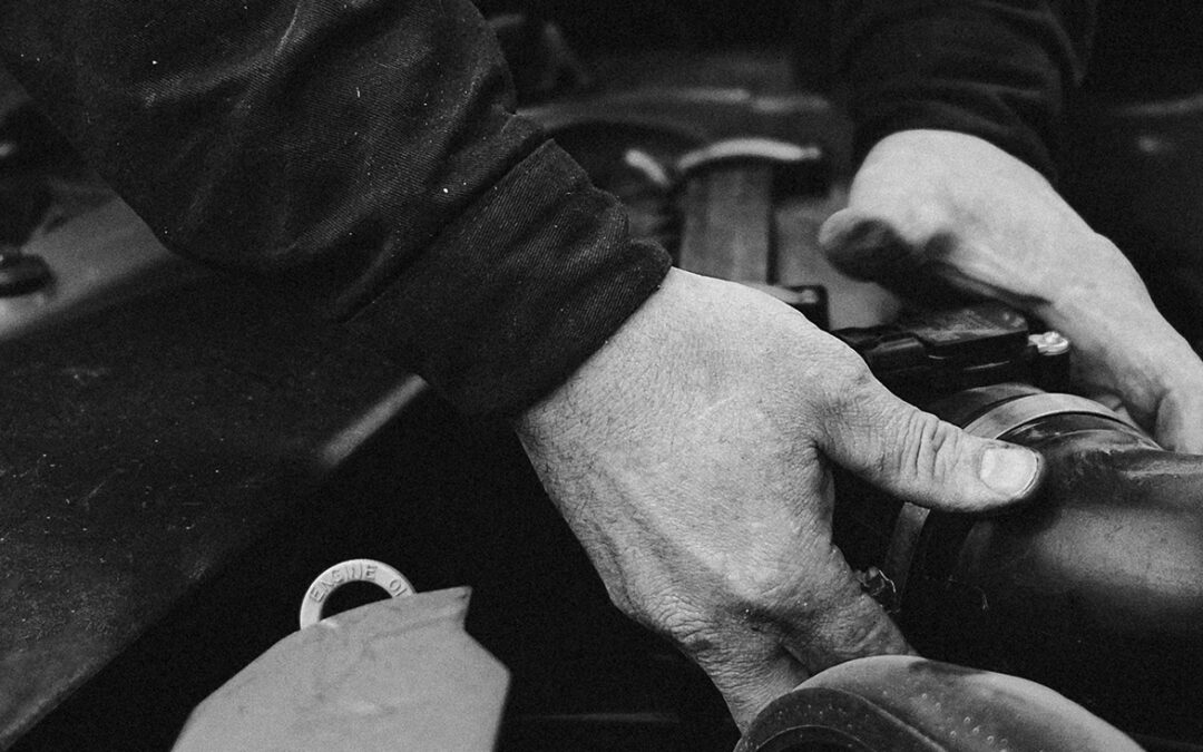 black and white photo of a mechanic under the hood of a car