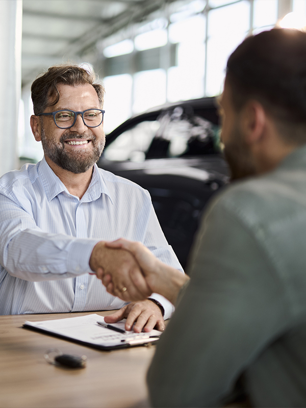 Two men smiling and shaking hands inside a car dealership